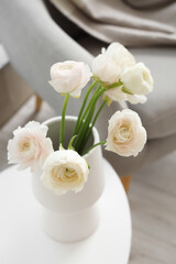 Vase with ranunculus flowers on table in living room, closeup
