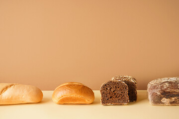 Loaves of different bread on beige table near brown wall