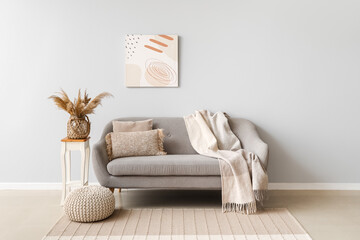 Interior of light living room with grey couch, table and pouf