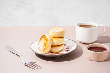 Plate with tasty cottage cheese pancakes, strawberry jam and cup of coffee on color table