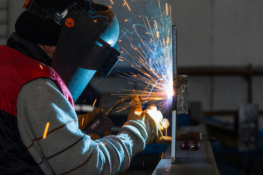 The welder is welding a structural steel with gas metal arc welding ( GMAW ) in the workshop.
