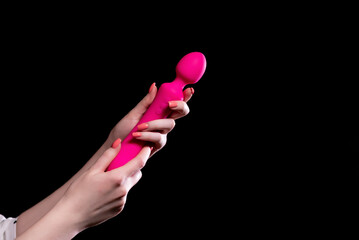 The girl's hand holds a pink massager for sex on a black isolated background. Vibrator for masturbation. Dildo for stimulation. Image for sex shop