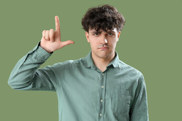 Young man showing loser gesture on green background