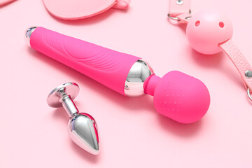 Vibrator with anal plug and mouth gag on pink background, closeup