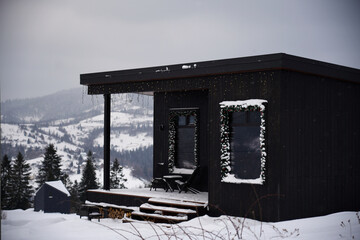 Decorated modern black small cottage on snowy mountains