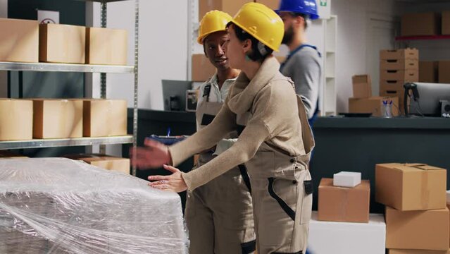 Diverse colleagues counting products on warehouse racks, looking at packages and doing inventory for merchandise goods. Young adult planning shipment for business distribution.