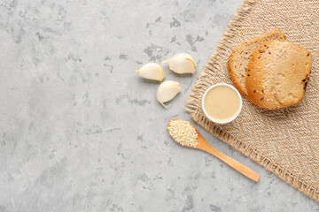 Bowl of tasty tahini, sesame seeds, garlic and bread on grunge background