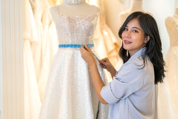 Portrait of entrepreneur bridal shop owner business woman fashion designer stylish working.Attractive designer girl using tape meter fitting on wedding dress with mannequin at wedding studio