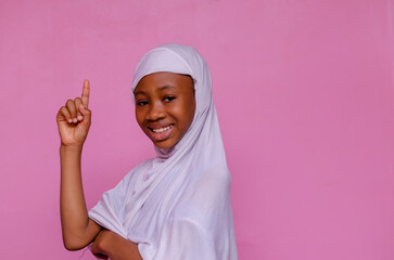 portrait of a pretty african Religious child smiling, pointing up with the other arm crossed