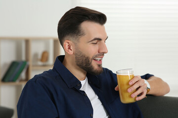 Handsome man with delicious smoothie on sofa at home