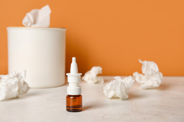 Fototapeta na wymiar Nasal drops with tissue box on table near orange wall, closeup. Allergy concept