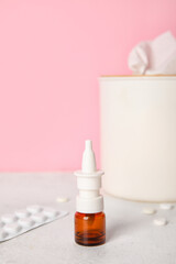 Nasal drops with pills and tissue box on table near pink wall. Allergy concept