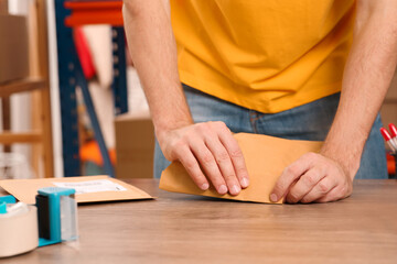 Post office worker sealing adhesive paper bag at counter indoors, closeup