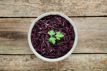 Obraz na płótnie Canvas Tasty red cabbage sauerkraut with parsley on wooden table, top view
