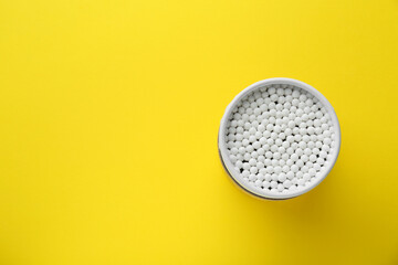 Container with new cotton buds on yellow background, top view. Space for text