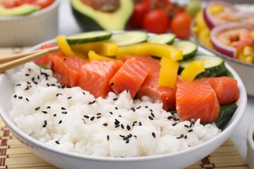 Delicious poke bowl with salmon, rice and vegetables on table, closeup