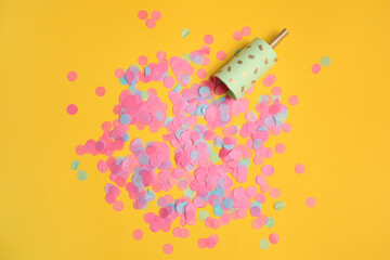 Party popper with bright confetti on orange background, flat lay