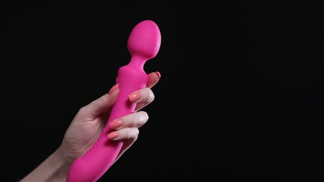 Girl holds in her hands a pink massager for sex on a black isolated background. Vibrator for masturbation. Dildo for stimulation. For sex shop
