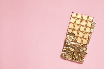 Shiny golden chocolate bar with foil on pink background, top view. Space for text
