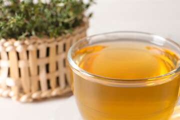 Aromatic herbal tea with thyme in glass cup on table, closeup