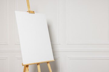 Wooden easel with blank canvas near white wall. Space for text - obrazy, fototapety, plakaty