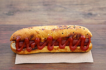 Fresh tasty hot dog with ketchup on wooden table, closeup