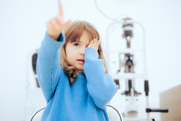Cute Little Girl Covering One Eye During Ophthalmological Consult. Toddler child pointing to a...