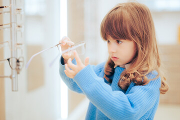 Little Girl Checking a Pair of New Eyeglasses in Optical Store. Toddler child choosing stylish...