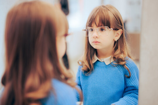 Little Girl Wearing New Eyeglasses Looking in the Mirror. Adorable fashionable toddler wearing stylish frames in optical store
