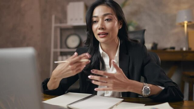 Professional Asian business woman in black suit working by talking with a partner team by using video call on laptop camera, online conference meeting by internet computer communication technology