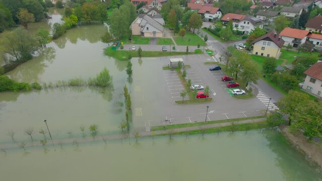 AERIAL: Parking lot in a small town is partially flooded due to river overflow. After heavy rains in autumn season, swollen river spilled over normal confines and inundated riverside with muddy water.