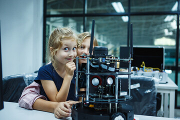 Fototapeta na wymiar Cute young girl smiling to the camera sitting in front of robot in robotics class in the classroom. Innovation technology and success concept.
