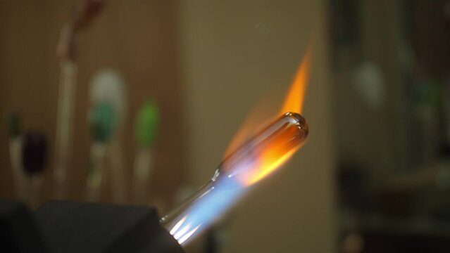 Silver glass artwork being heated in fire by glass blowing artist