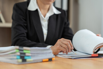 Financial advisor, analyst, asian businesswoman pointing at financial statistics report paper business income Taxes piled up on the desk to validate presentations at office meetings.
