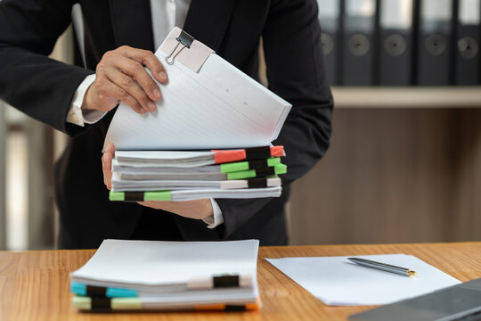 Businesswoman in black suit working at desk with documents preparation, searching, sifting through information related to financial, earnings, taxes of company to prepare for meeting in office.