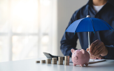 Businessman, Retirement Age, Teenager, Financial Strength, Protection Piggy bank with umbrella hand holding and pile of coins money, financial insurance and safe investment concept. © Phimwilai
