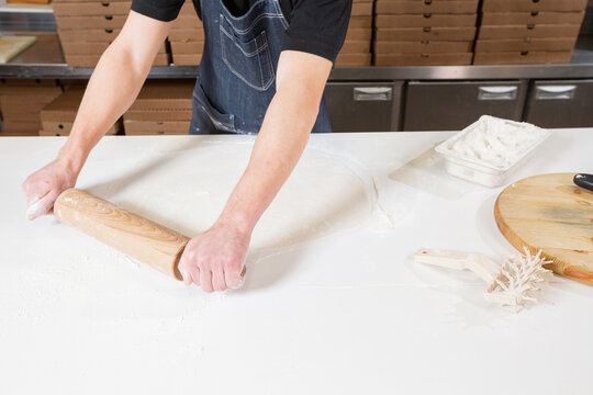 Dough for pizza, the chef rolls out the blanks. Closeup hand of chef baker in uniform white apron cook pizza at kitchen