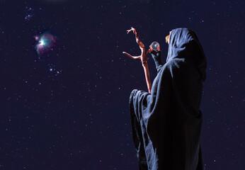 A fortune teller stands outside at night with her crystal ball and looks at the starry sky