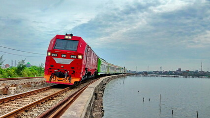 Fototapeta premium Special Train with Red Locomotive Runs on The Side of The Lake at Semarang City