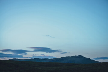 Beautiful twilight landscape with blue clear gradient sky over lilac violet clouds above silhouettes of mountains and hills with rocks. Atmospheric minimalist scenery with mountain silhouettes in dusk