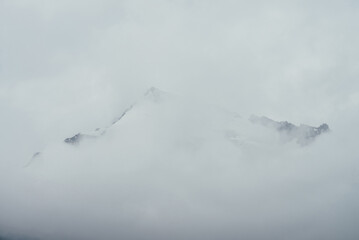 Minimal mountain landscape with high pointy rock in clouds. Minimalist mountain scenery with sharp snowy mountain peak over clouds. Snow-white pointed pinnacle above white clouds. Big top in dense fog