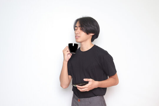 Portrait of handsome Asian man in black t-shirt drinking a cup of coffee while holding the saucer. Isolated image on white background