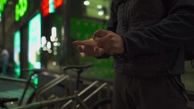 Male cyclist disinfects his hands with antiseptic after shopping, wears helmet, and going to leave in evening in city. Masked cyclist sprays sanitizer sprayed on his hands at night near supermarket. 