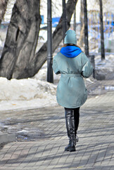 A young woman walks along the sidewalk on a spring day