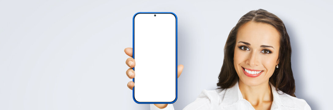 Image of excited smiling young woman in confident cloth, holding show smartphone cell phone mobile with white blank mock up screen, isolated grey gray background. App application ad