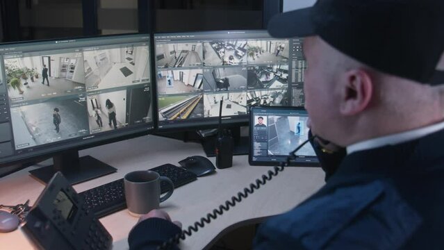 Security officer controls CCTV cameras with facial recognition in office, uses digital tablet and computers. High tech software with surveillance cameras playback on screens. Concept of social safety.