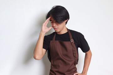 Portrait of attractive Asian barista man in brown apron holding hand on forehead, forgets...