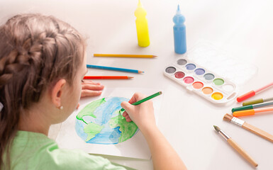 A girl draws the planet Earth on a sheet of paper with a colored pencil