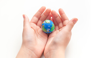 Hands of a child holding a small globe made of plasticine on a white background