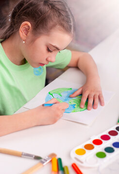 A girl in a green shirt draws a map of the world.
